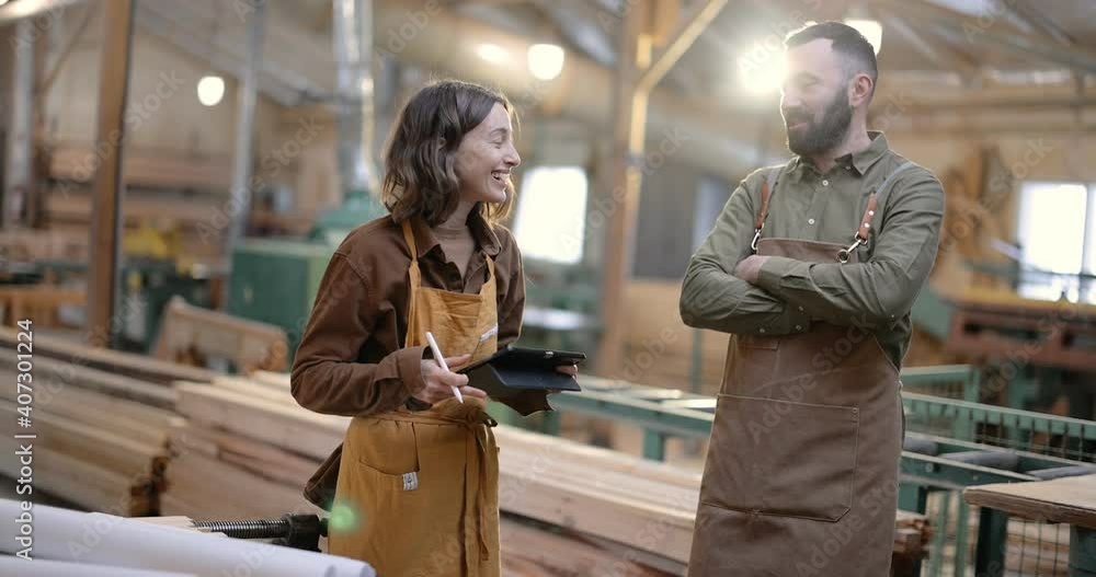 Cheerful carpentry workers discuss some working moments with a digital tablet at the manufacturing. Happy colleagues at the factory Cheerful carpentry workers discuss some working moments with a digital tablet at the manufacturing. Happy colleagues at the factory