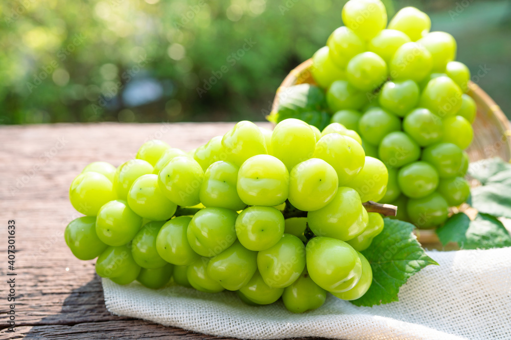 Green grape in Bamboo basket on wooden table in garden, Shine Muscat Grape with leaves in blur background Green grape in Bamboo basket on wooden table in garden, Shine Muscat Grape with leaves in blur background