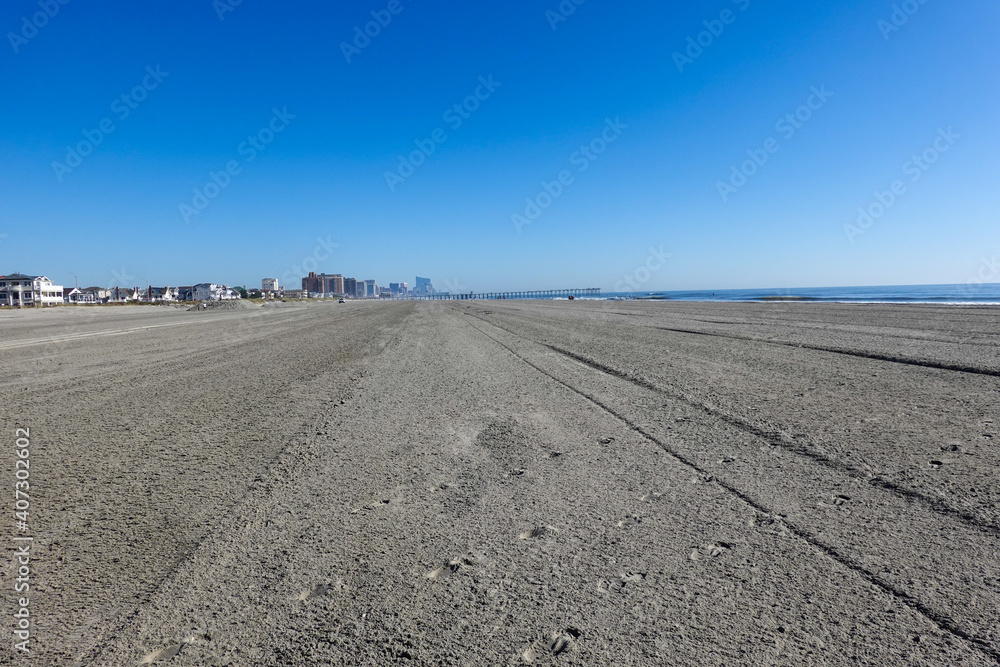 View up a huge empty beach with tire tracks towards several large buildings in the distance