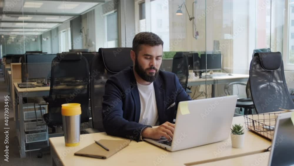 Zoom-in medium shot of serious mixed race business man working on laptop in empty open space office Zoom-in medium shot of serious mixed race business man working on laptop in empty open space office