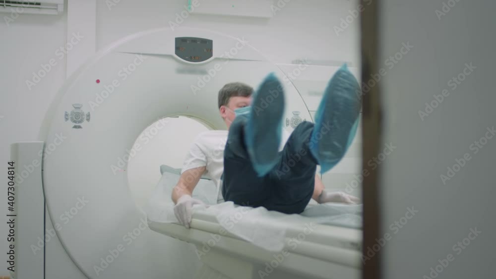 A patient in a protective medical mask lies in a modern computed tomography apparatus. The doctor analyzes the lungs on a CT scanner. The danger of covid or coronavirus. Human lung scans A patient in a protective medical mask lies in a modern computed tomography apparatus. The doctor analyzes the lungs on a CT scanner. The danger of covid or coronavirus. Human lung scans