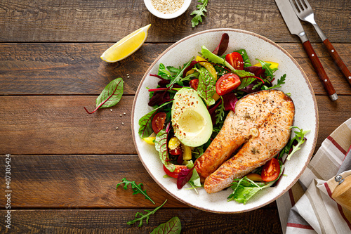 Salmon fish steak grilled, avocado and fresh vegetable salad with tomato, bell pepper and leafy vegetables. Top view