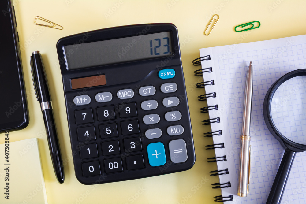 Calculator, notebook and pen on a yellow surface Calculator, notebook and pen on a yellow surface