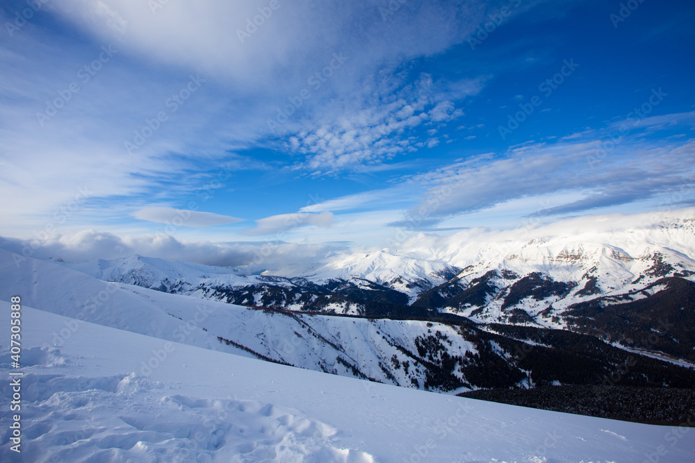 Snow peaks of mountains with blue sky and beautiful clouds. Winter tourism in Russia, Arkhyz. Snow valley on horisontal landscape. Snow peaks of mountains with blue sky and beautiful clouds. Winter tourism in Russia, Arkhyz. Snow valley on horisontal landscape.