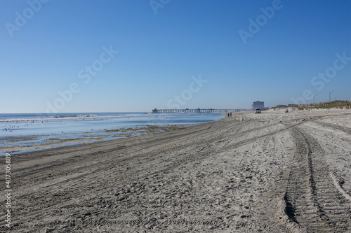 View down a empty beach with tire tracks towards a white truck and several people in the distance