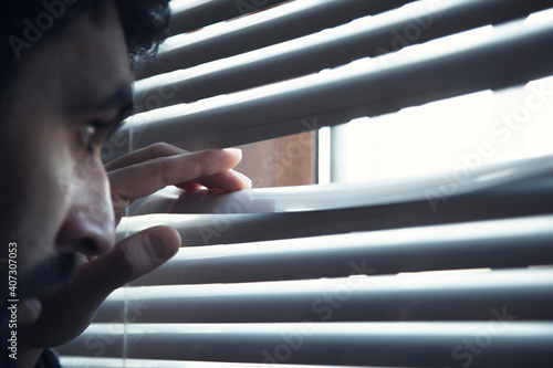 Young man opening window blinds