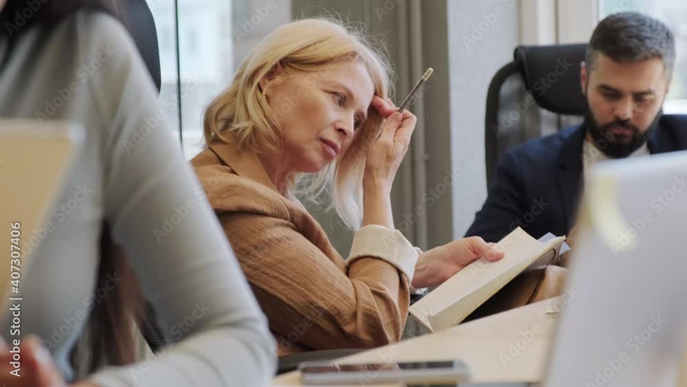 Medium close-up of adult caucasian woman making notes in notebook working among diverse colleagues in modern open space office Medium close-up of adult caucasian woman making notes in notebook working among diverse colleagues in modern open space office