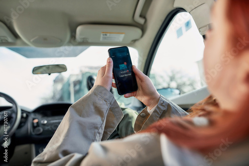 Portrait of teenage girl holding smartphone in her hands, sitting in the car. New message from her boyfriend on the screen. The concept of smartphone addiction