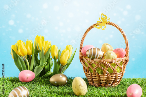Basket of multicolored easter eggs with tulip flowers on green meadow over blue background with bokeh.
