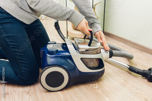Obraz na plátně Woman takes dust filter out of vacuum cleaner at home