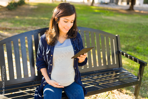 Smiling pregnant woman using a tablet in the park