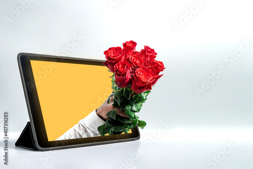 Hand holding out a bouquet of roses from the tablet screen. A male hand reaching out from tablrt screen, holding bouquet of red beautiful roses photo