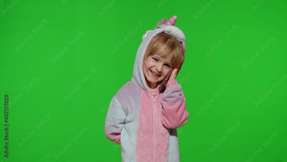 Smiling little kid girl daughter in unicorn pajamas using speaking talking on mobile cell phone with mother isolated on chroma key green background in studio. People family lifestyle. Copy space Smiling little kid girl daughter in unicorn pajamas using speaking talking on mobile cell phone with mother isolated on chroma key green background in studio. People family lifestyle. Copy space