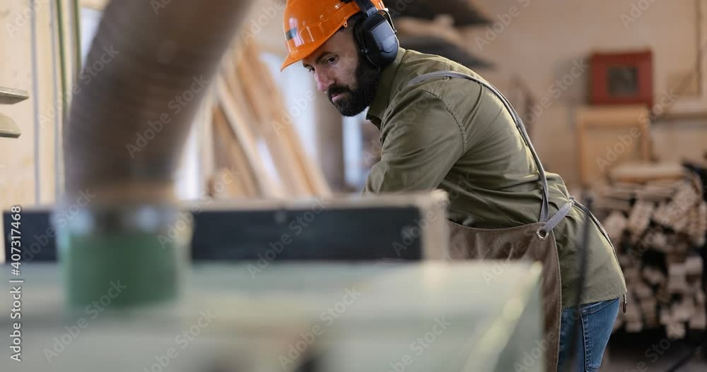 Carpnertry factory worker in hard hat cuts boards on a sawmill. Woodworking industry Carpnertry factory worker in hard hat cuts boards on a sawmill. Woodworking industry