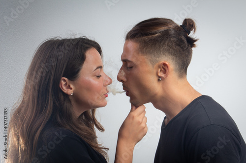 Loving young couple share the smoke of a cigarette. Boyfriend and girlfriend isolated on grey background 