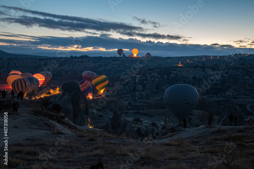 Hot air balloons glowing in dark early morning while inflating on land of mountain landscape in Cappadocia Turkey. Colorful illuminated air balloons among volcanic rocks