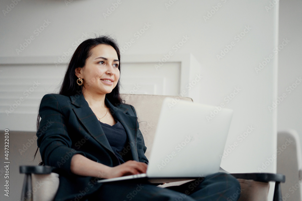 prints text on a laptop. a brunette businesswoman sits in a chair and smiles. Good mood great go up things on the project at work. Stylish, bright, modern office in the city center. prints text on a laptop. a brunette businesswoman sits in a chair and smiles. Good mood great go up things on the project at work. Stylish, bright, modern office in the city center.