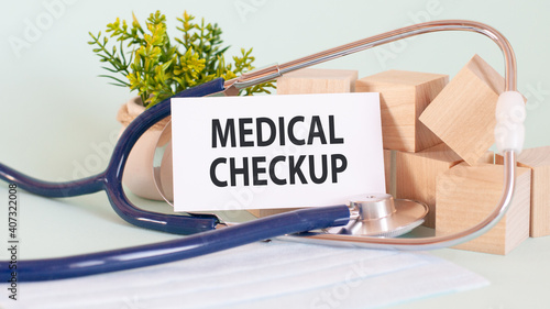 Card with words MEDICAL CHECKUP, stetoscop, wooden blocks and flower on table photo