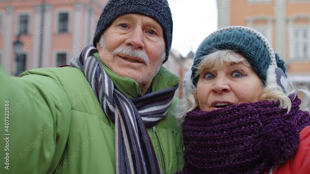 Couple of senior tourists taking selfie in winter city center smiling, looking at camera. Elderly grandmother, grandfather enjoying conversation, video call, blog, vlog. Tourism and pensioners concept Couple of senior tourists taking selfie in winter city center smiling, looking at camera. Elderly grandmother, grandfather enjoying conversation, video call, blog, vlog. Tourism and pensioners concept