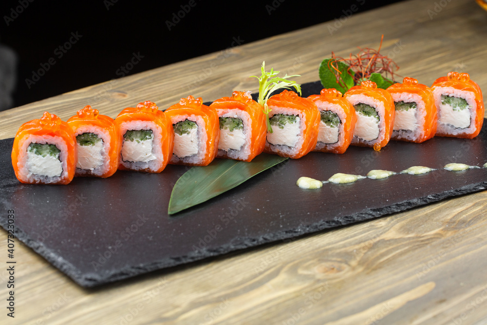 Close-up of uramaki sushi rolls with red caviar, salmon, tuna, cucumber and avocado isolated on black background. Delicious traditional japanese food with sushi rolls.