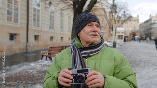 Portrait of senior man taking pictures with photo camera, smiling using retro device outdoors in winter city center of Lviv, Ukraine. Photography, travelling, vacation. Active life after retirement