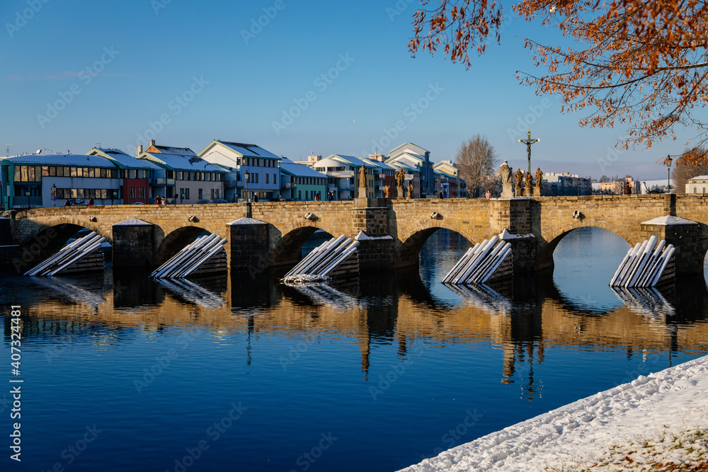 Gothic medieval Stony Deer bridge with show, Riverbank of the Otava river in winter sunny day, the oldest bridge in historical royal town Pisek, South Bohemia, Czech Republic