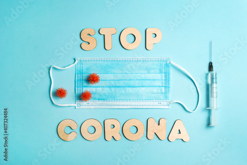 Words STOP CORONA 19 from wooden letters, syringe with vaccine on blue background, and facemask. Vaccination and the end of epidemic concept. Vertical.