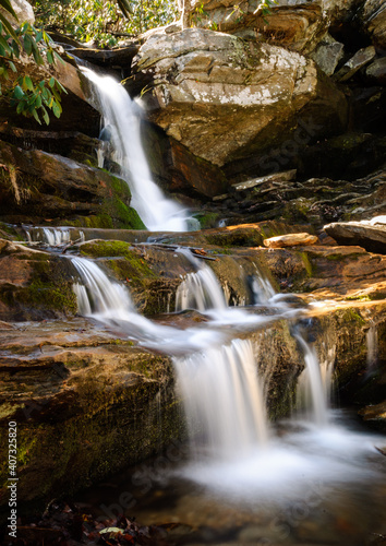 Small waterfall cascades over sunlit rocks in summer forest