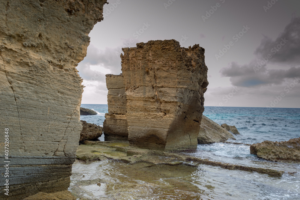 A beautiful landscape view of sedimentary sandrock rock formations by the blue green sea on a cloudy day at the impressive coast of mediterranean llucmajor in Mallorca island spain balearic