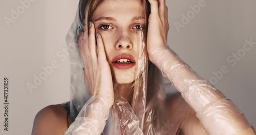 Woman abuse. Domestic violence. Female rights. Art portrait of sensual hurt lady with full lips wearing polyethylene film touching head suffering from humiliation isolated on beige background.