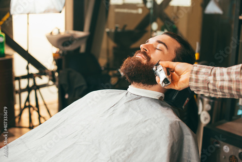 Photo of bearded man at barbershop making clean beard haircut.