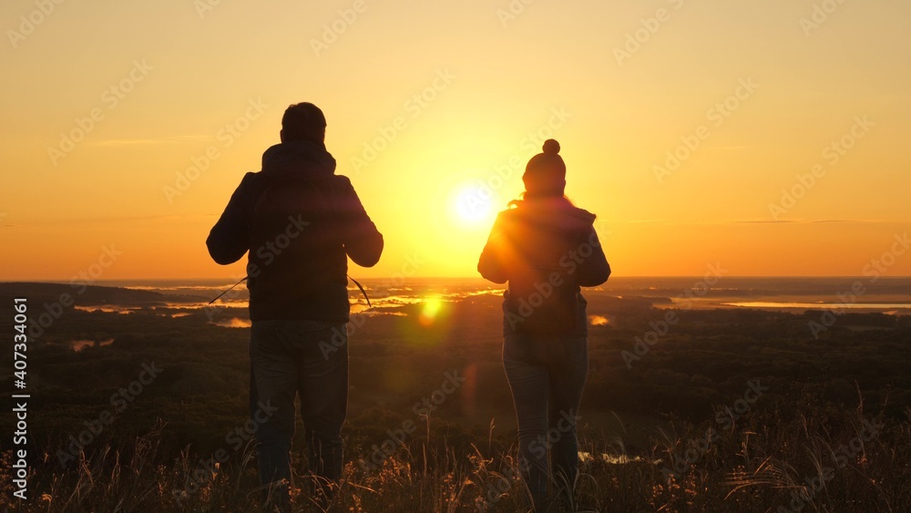 Carefree tourists travel at sunset. Teamwork in business. Free travelers, a man and woman with backpacks, descend from mountain in rays of dawn, enjoy nature, beautiful sun and landscape.