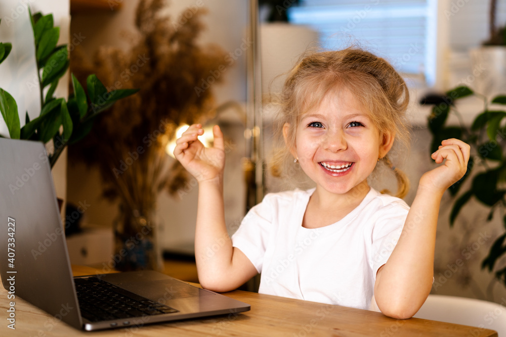 Fototapeta premium a small blonde girl with a laptop sits at a table and smiles