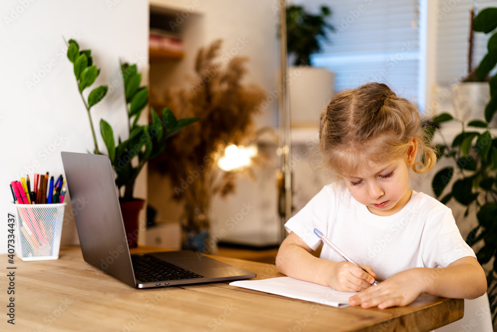 serious girl laughing at her laptop and doing homework in a notebook, home learning concept in the covid 19 pandemic serious girl laughing at her laptop and doing homework in a notebook, home learning concept in the covid 19 pandemic