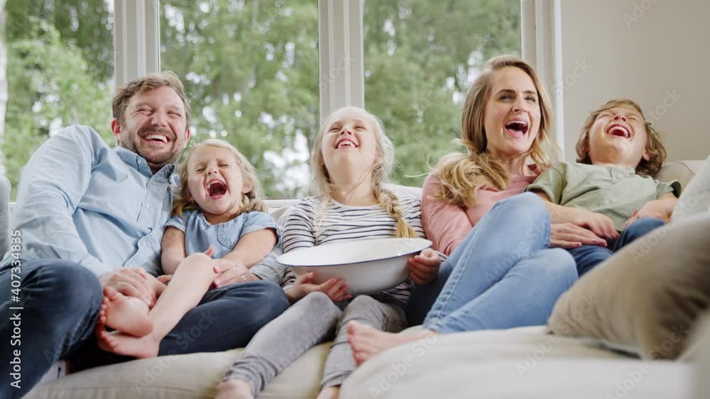 Family sitting on sofa at home laughing and watching TV with popcorn together - shot in slow motion Family sitting on sofa at home laughing and watching TV with popcorn together - shot in slow motion
