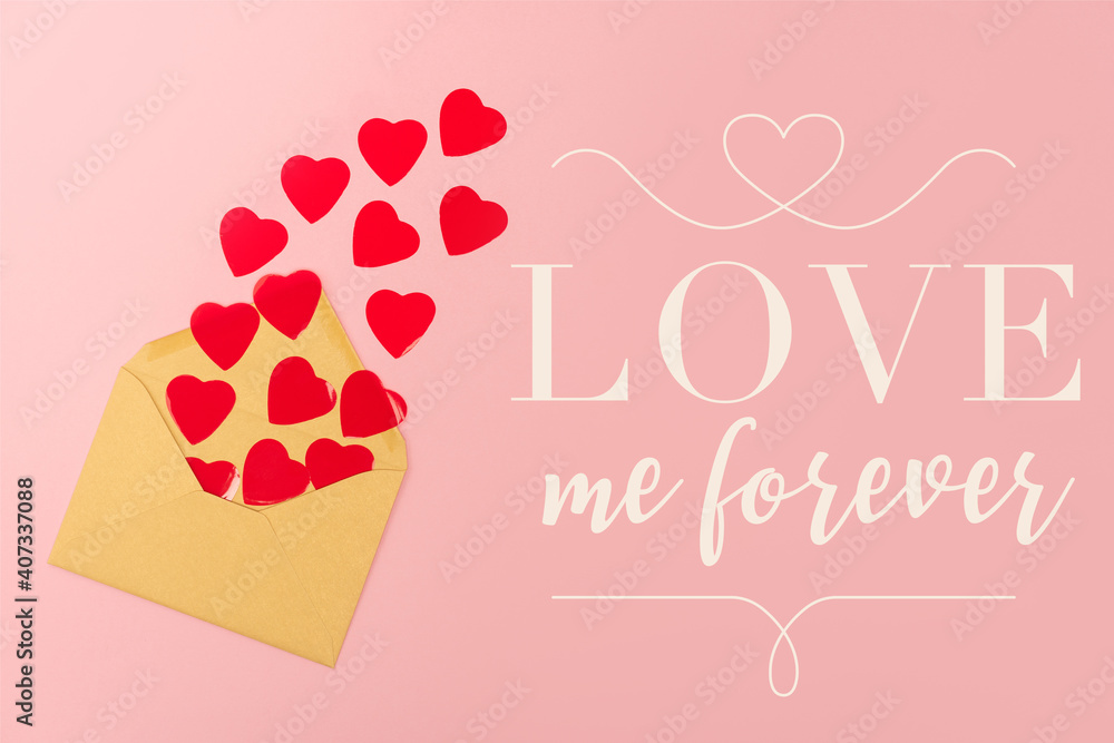 top view of red paper hearts and envelope near love me forever lettering on pink background