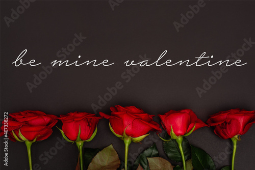 Top view of red roses near be mine valentine lettering on black