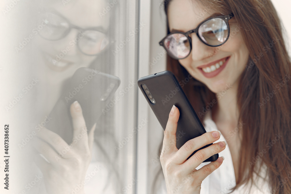 Girl in a office. Woman in a white shirt. Lady in a glasses standing by the window.