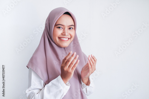 Asian Islam Muslim woman in headscarf and hijab prays with her hands up in air with smile face. Indonesian woman. Religion praying concept isolated on grey background