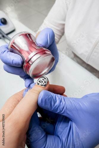 selective focus process of manicure in salon, gloved hands make decor on white nails with stamping. compliance with measures when performing, vertical content