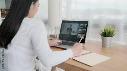 Online classroom video call with classmates and professor teaching educational learning, social distancing working from home workspace, happy smiling Asian girl writing on note book revising studying