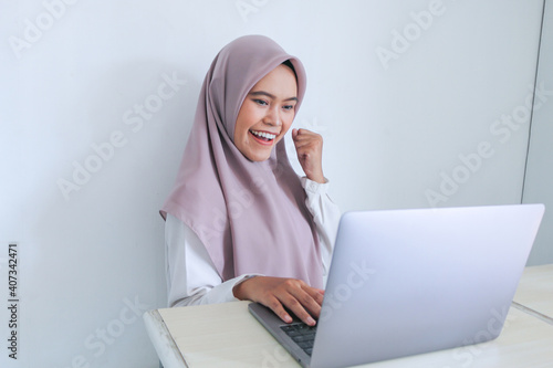 Young Asian Islam woman wearing headscarf is happy and excited celebrating in what she see on the smartphone. Indonesian woman on gray background
