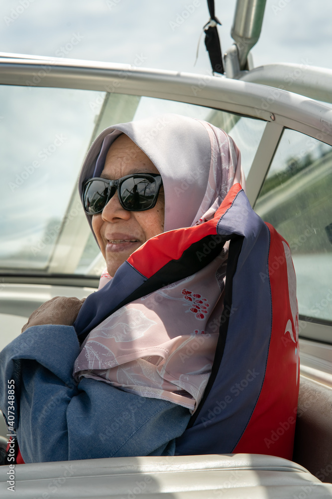 Naklejka premium Senior muslim woman wearing sunglasses on wearing life jacket on the boat.