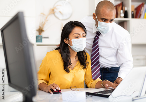 Manager in protective medical mask gives task to assistant at office