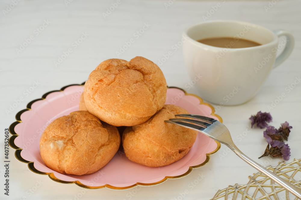 Homemade choux cream or Choux Pastry or Profiterole or Eclair or cream puff on pink plate near the dessert fork serve with tea or coffee. French dessert concept. selected focus. Homemade choux cream or Choux Pastry or Profiterole or Eclair or cream puff on pink plate near the dessert fork serve with tea or coffee. French dessert concept. selected focus.