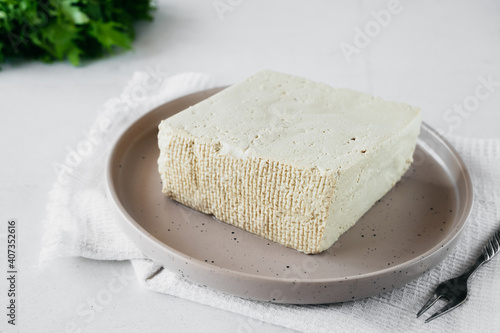 tofu cheese is large piece on plate with cheese fork and cotton napkin on white background. Healthy dietary vegetarian food, selective focus