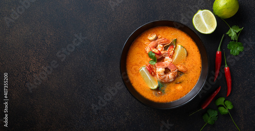 Tom Yam kung Spicy Thai soup with shrimp in a black bowl on a dark stone background, top view, copy space