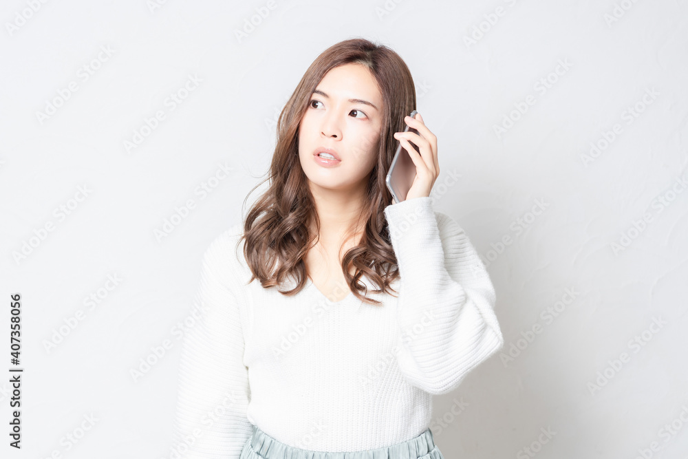 白い壁の前に立って、スマホを使う若い女性 白い壁の前に立って、スマホを使う若い女性