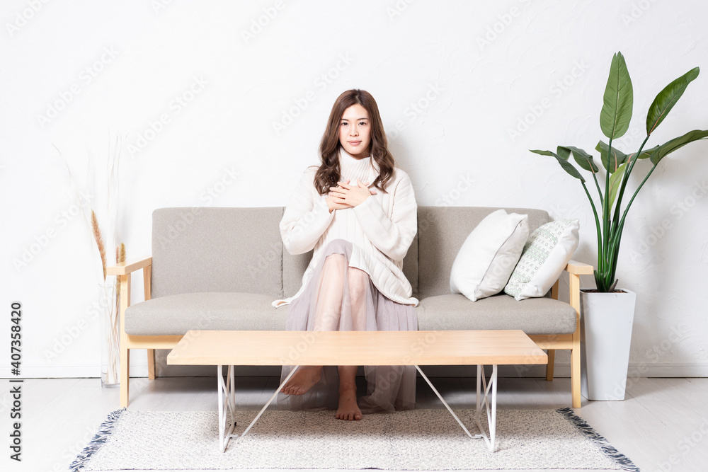 リビングのソファに座って、胸に手を当てる若い女性