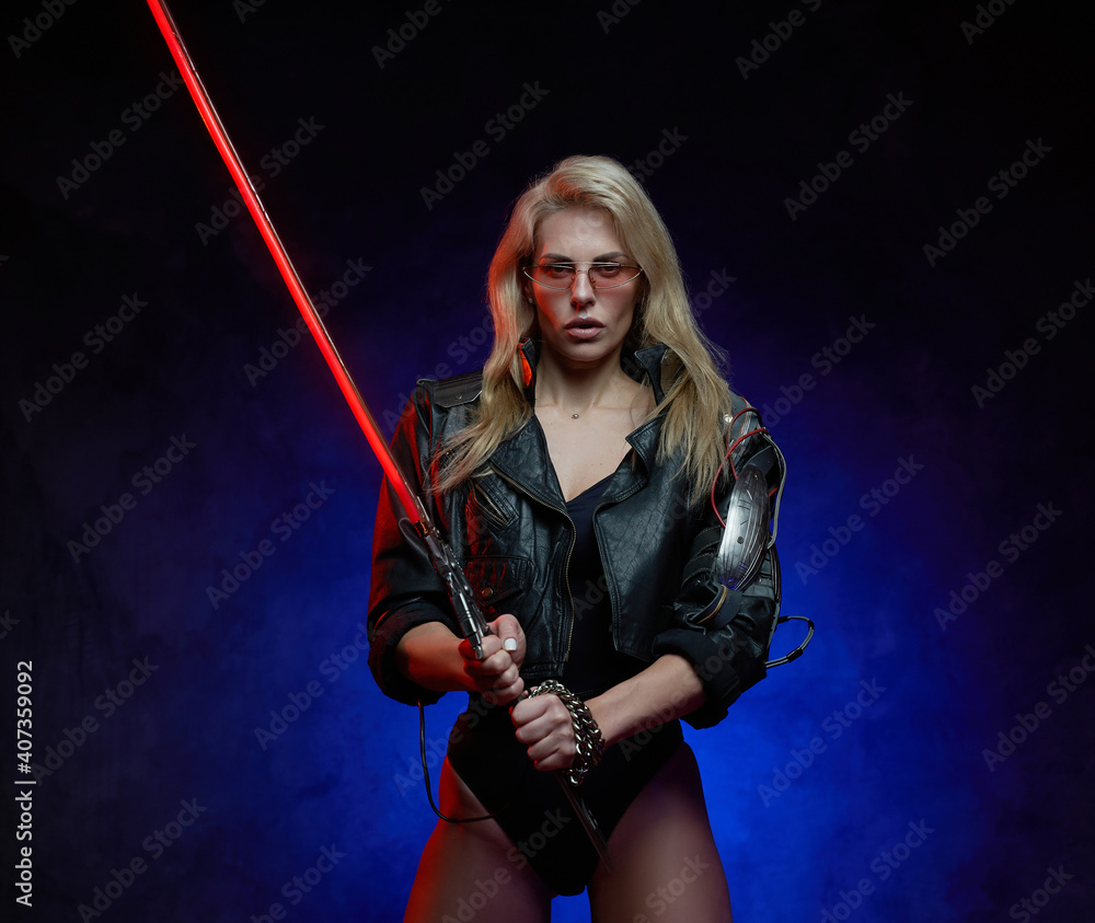 Martial woman with blond hairs and cybernetic hand holds her glowing sword looking at camera in blue background. Martial woman with blond hairs and cybernetic hand holds her glowing sword looking at camera in blue background.